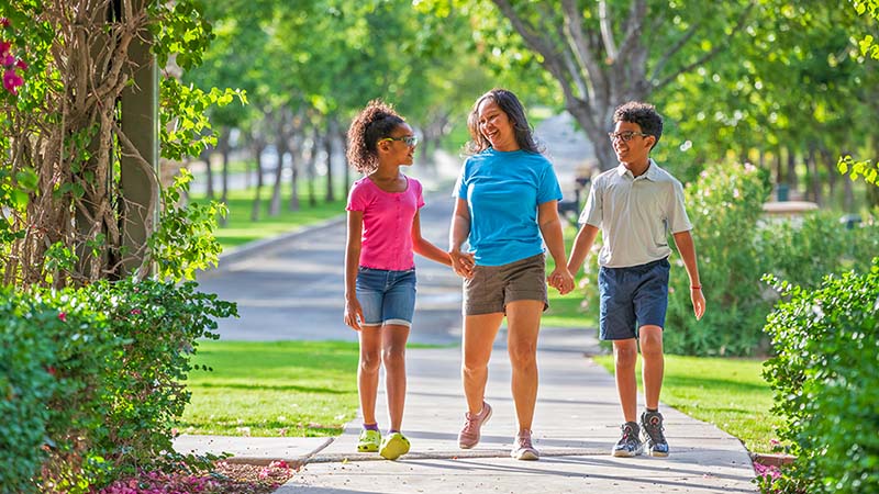 A woman holds hands with her son and daughter as they walk down a sidewalk in their new neighborhood. The answer to “how often do military families move” is about 2.5 years.
