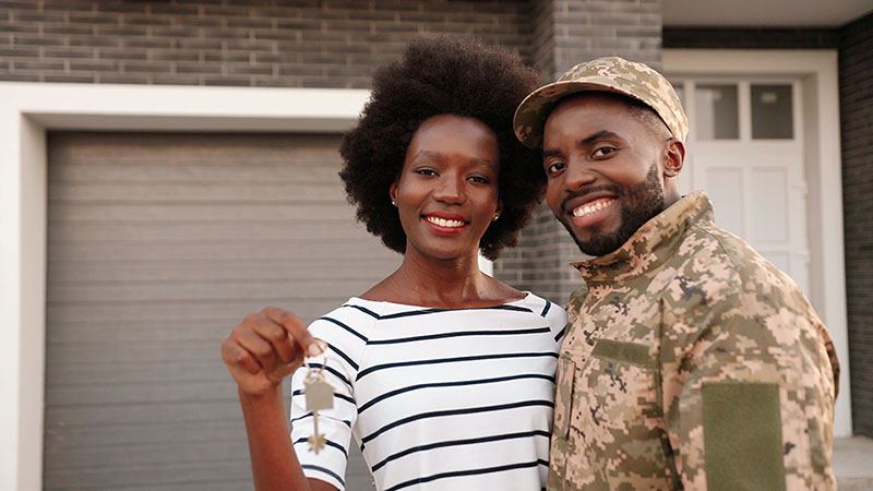 A military couple stands in front of their new home. The woman is holding the keys to their new home.