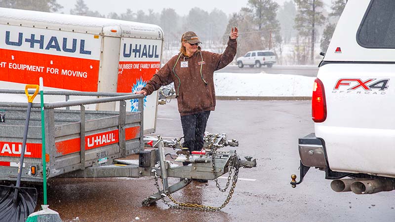 A U-Haul employee helps a customer get their vehicle lined up with the U-Haul cargo utility trailer as she gives the customer hand signals on a winter day.
