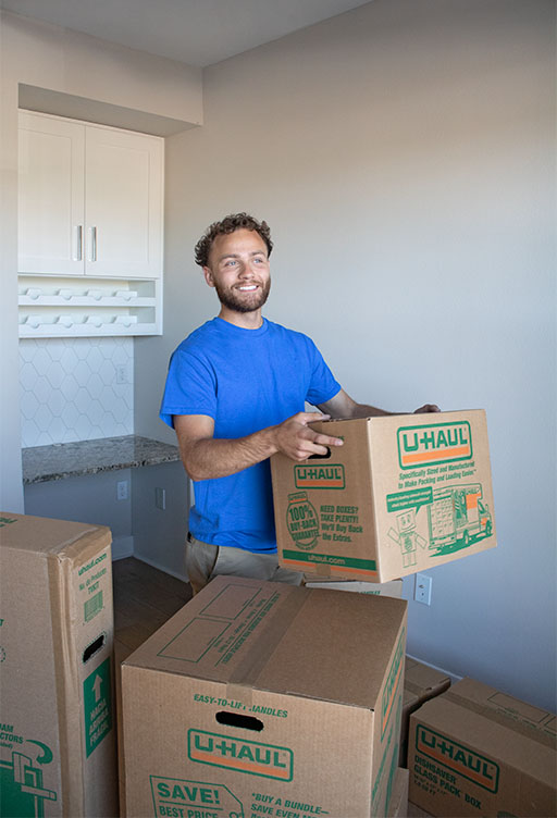 A moving labor provider lifts a U-Haul small moving box in the living room to carry it to a customer’s U-Box storage container outside.
