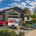 A couple begins unloading their belongings from a U-Haul cargo trailer that they towed using their car.