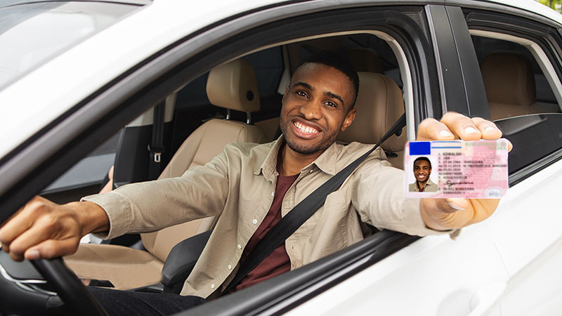 A man sits in his car as he holds his new driver’s license that he got after moving to a new state.
