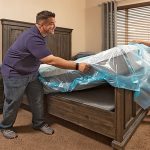 A couple works together to take off a mattress cover off their mattress in their master bedroom.