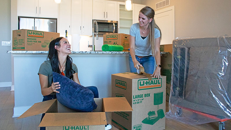 Two women work together to pack pillows and other items into their U-Haul moving boxes to prepare for a move.