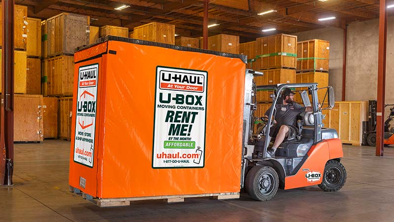 A U-Haul employee carefully uses a forklift to move a U-Box storage container at a U-Haul center.