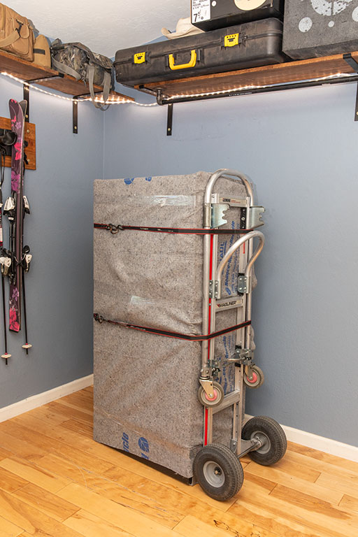 A customer’s gun safe is wrapped in furniture blankets while sitting on a dolly in a room where a customer just cleaned the baseboards.
