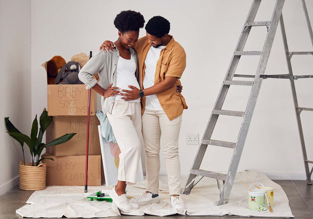 A couple stands together while the husband feels the baby move in the mother’s womb. The couple works together to paint and move boxes in the baby’s new room.
