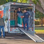 Two Moving Help Service Providers unload a couple’s belongings out of a U-Haul truck rental while the couple watches.