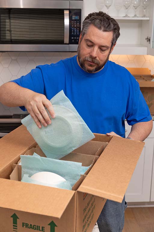 A Moving Help Service Provider begins taking plates out of a kitchen moving box for a customer.