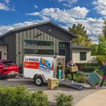 A couple unloads items out of their U-Haul cargo trailer and into their new home that they bought together.