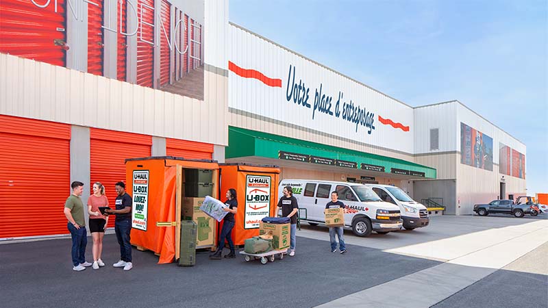 Three Service Providers load a military couple’s belongings into a U-Box storage container while a fourth Moving Helper talks to the couple watching the load.