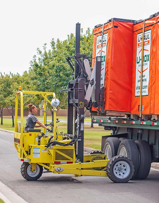 A U-Haul employee uses a forklift to carefully unload a U-Box storage container off a U-Haul truck transporter.