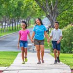 A mom walks down a sidewalk with her daughter and son as they talk to one another while holding hands.