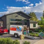 A man and a woman work together to unload their U-Haul cargo trailer and move their belongings into their new house rental.