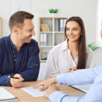 A male landlord points to the couple at their leasing document to show them where their rent concession is located as the couple signs the leasing agreement.