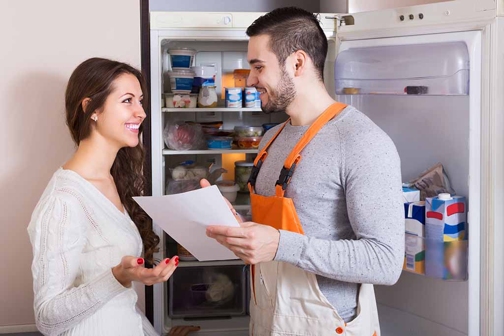A maintenance man talks to a female tenant while pointing to a piece of paper he’s holding, going over a list of maintenance requests in her apartment.