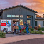 A boyfriend and a girlfriend use forearm forklift moving straps to move a dresser out of their U-Haul truck rental and into their new home.