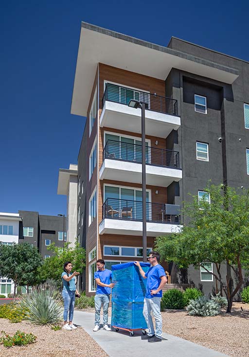 A customer provides directions to her two Moving Help Service Providers who are pushing a piece of furniture on a furniture dolly and into the couple’s new apartment.
