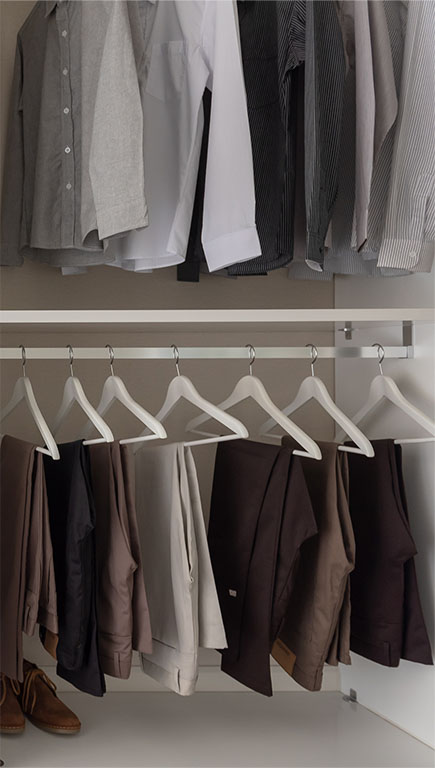 Shirts hang from a tall clothing rod in a closet. Pants hang from a lower rod below it.
