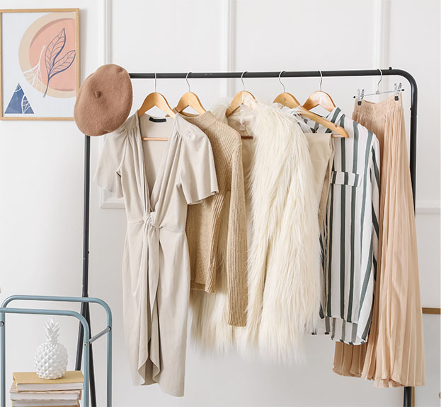 A robe, beret, and elegant clothing hang on a display on a clothing rack in the bedroom.