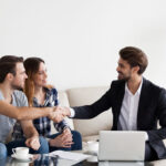A male realtor shakes hands with the husband as the husband and wife talk to their realtor.