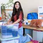 A college student unpacks her college essentials and belongings from a plastic tub inside her college dorm room.