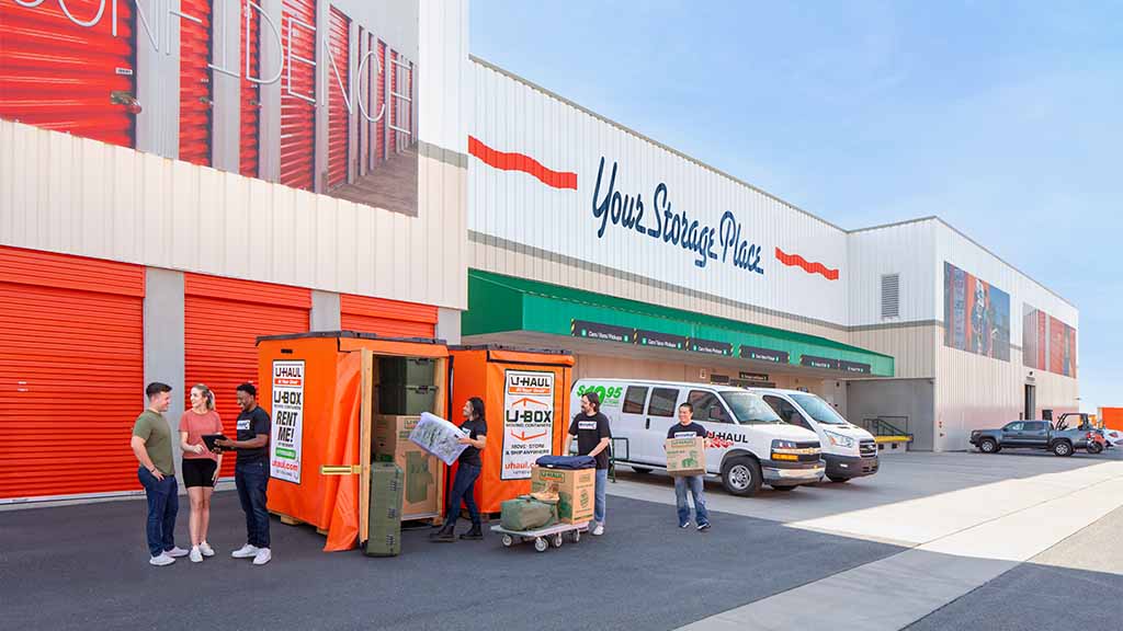 A Service Provider discusses a couple’s move with them. Behind them, three providers carry moving boxes into a U-Box storage container at a U-Haul center.