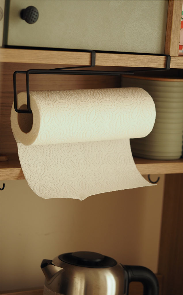 A roll of paper towels hooks onto a metal paper towel holder, which hangs from the base of a tall kitchen cabinet.