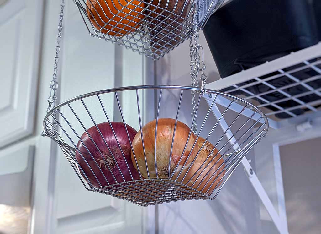 Oranges and onions fill each tier of a metal fruit basket which hangs from a kitchen ceiling in a tiny kitchen.