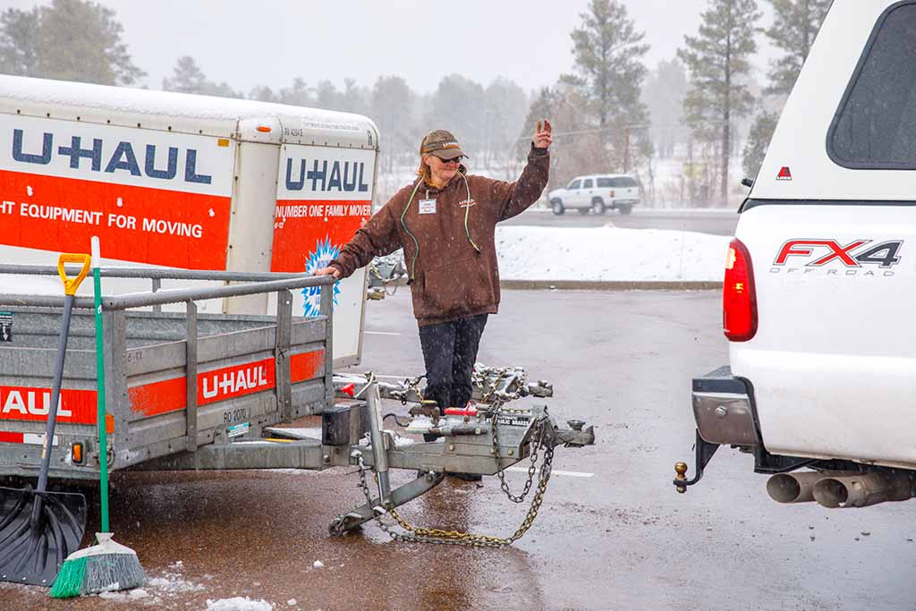 A U-Haul employee helps a customer hook up a U-Haul utility trailer to a customer’s car in the middle of a snowy winter day.