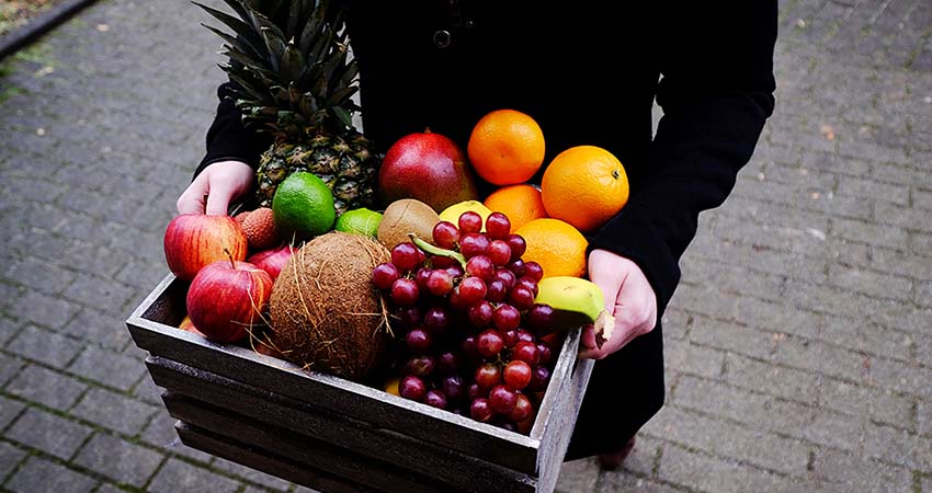 A woman carries a crate of fruit. Food or snack subscriptions are great going away gifts.