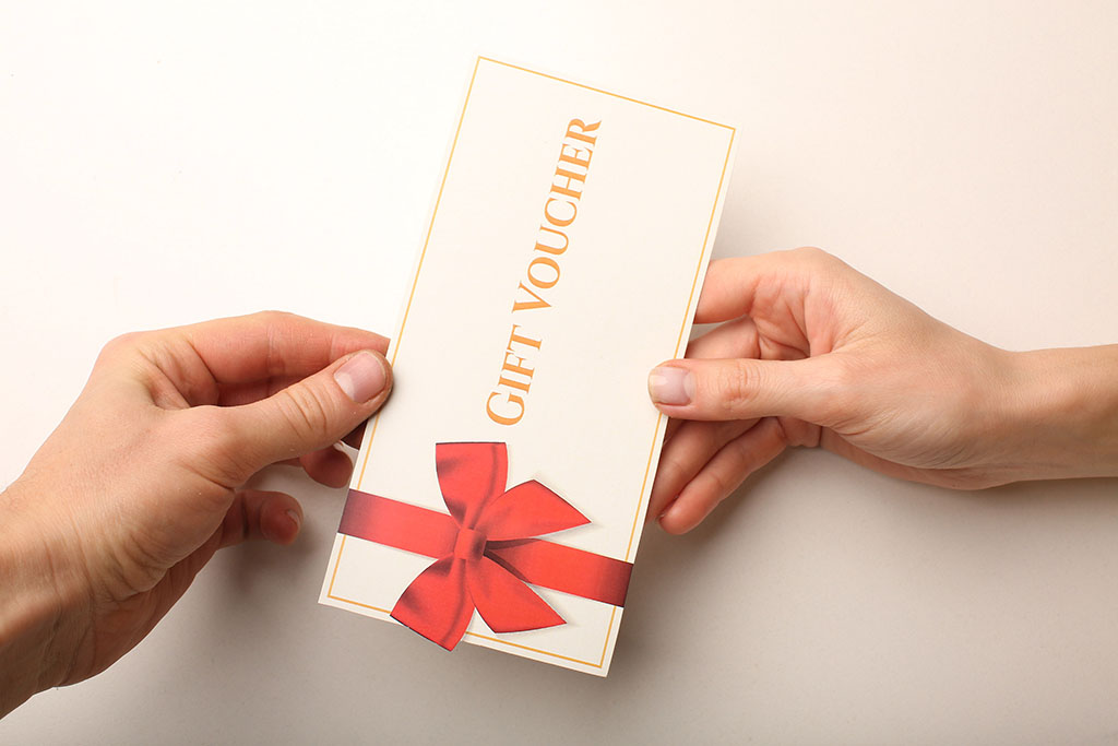 Two hands are shown as one hand passes a gift voucher to another person’s hand.