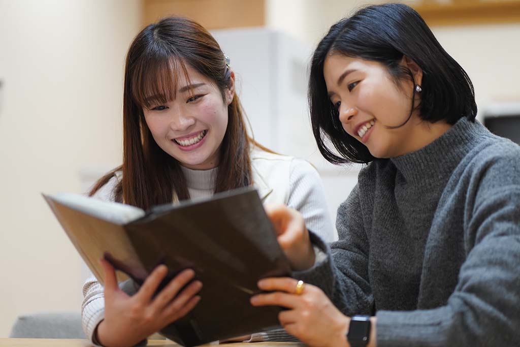 Two women smile as their reminiscence memories from the printed photo book. Online or print photo books are great going away gifts.