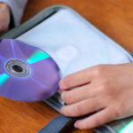A man carefully places a DVD into a DVD cover case. Knowing how to store DVDs doesn’t have to be a difficult task.