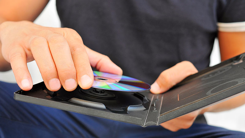 A man places a DVD back into its DVD case. Knowing how to store DVDs doesn’t have to be a difficult task.