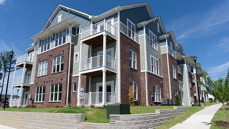Townhouses line next to one another while being surrounded by grassy areas and a sidewalk.