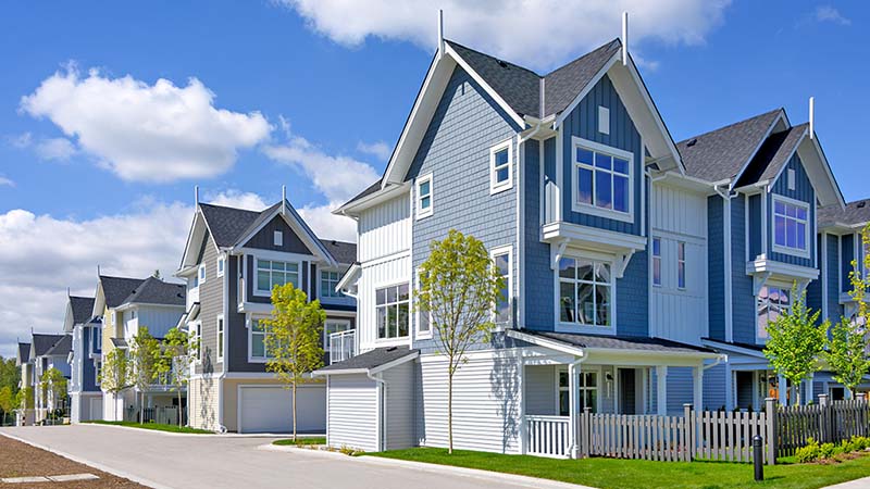 Townhouses sit next to one another. Some townhouses have garages while other townhouses have a small-fenced backyard.