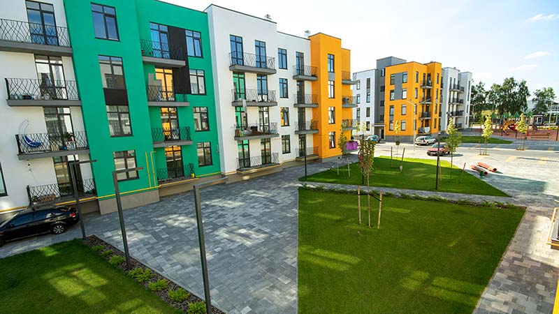 Townhouses in different colors line next to one another. On the ground floor, residents can walk a tiled concrete ground or the grassy areas in the community.
