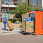 Two Moving Help Service Providers carefully load small moving boxes and a TV moving box into a U-Box storage container.