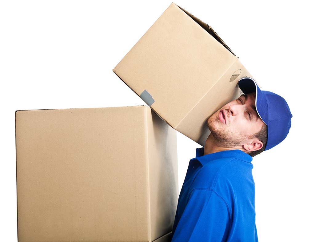 A mover struggles to carry two moving boxes. The top moving box is about to tip over and rests on the mover’s cheek to keep its balance.