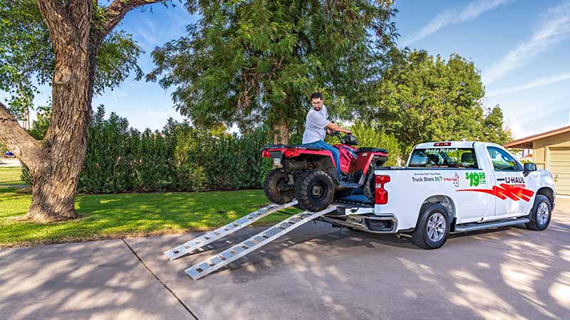 A man carefully unloads his ATV off his U-Haul pickup truck at his house.