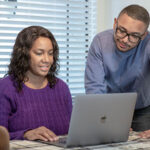 Two parents look at an Apple computer at the dining table as they prepare for moving during the school year.