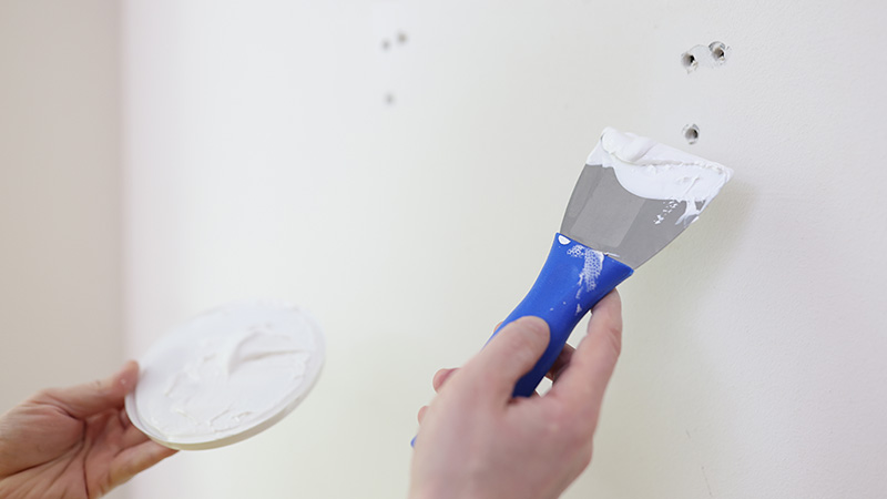 A woman begins to spackle three nail holes on her wall.
