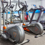 A modern gym interior features two elliptical machines and two treadmills facing a mirrored wall. The bright, clean space conveys a sense of energy and readiness.