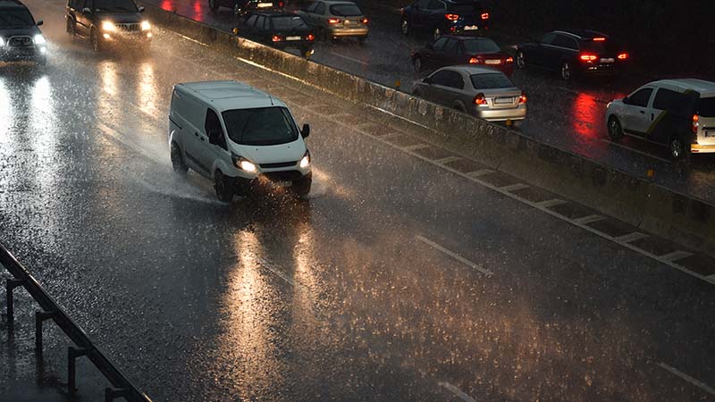 A van and multiple cars slowly drive on a rainy road in the city. If you don’t plan ahead, moving in bad weather can delay your move-in date.