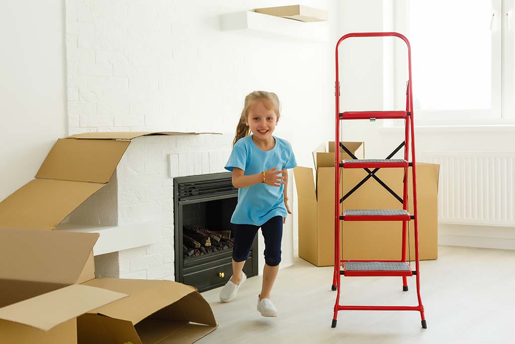 A child runs around in a room as she avoids the moving boxes and a ladder. Moving students in elementary school can be easier if you plan ahead with your child.