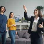 A real estate agent shows the living room of a house to a man and a woman. The couple looks interested in the home.
