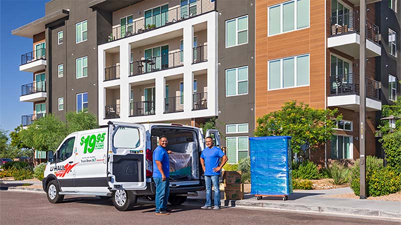 Two Moving Helpers stand near a U-Haul cargo van outside a customer’s apartment building.