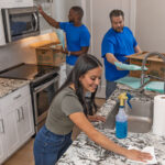 Two Moving Helpers carefully pack plates and glass cups for a customer. Rather than trying to learn how to pack fragile items for moving, a female customer hired helpers while she cleans her kitchen.