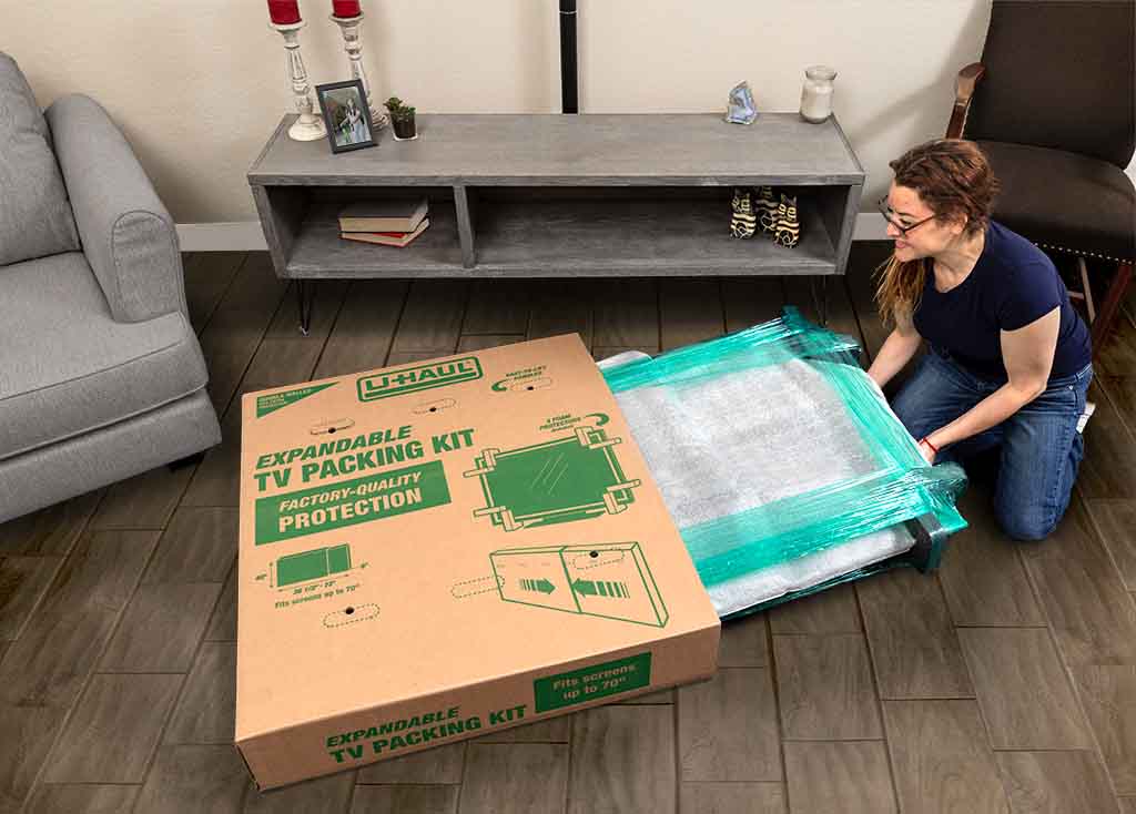 A woman gently puts a picture into a TV moving box. Preparation is key for when learning how to pack fragile items for moving.